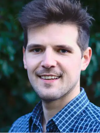 Profilfoto von Psychologe Maximilian König, lachend in blauem, kariertem Hemd – Fachkompetenz und Empathie in der psychologischen Beratung und Therapie.