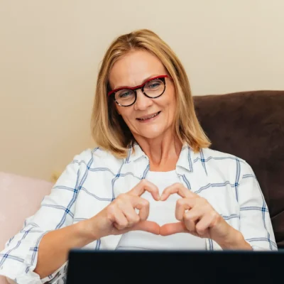 Frau zeigt Herzsymbol durch Laptop und lacht – Online-Psychotherapie (HPG) bei Psychologe König für vertrauensvolle und empathische Beratung und Therapie.