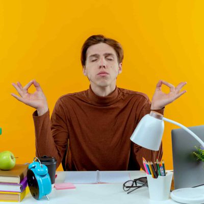 Schüler oder junger Arbeitnehmer meditiert an Schreibtisch mit Schulmaterialien – Maximilian König bietet Beratung für Stressbewältigung in Schule und Arbeitsplatz.
